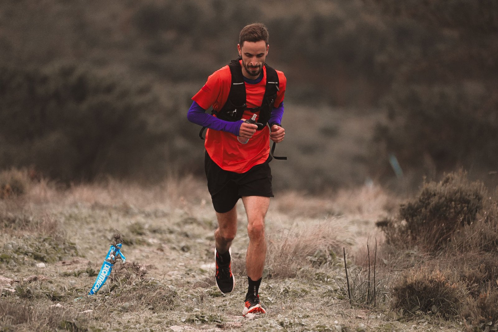 Coureur en tenue rouge sur un sentier de terre, montre GPS au poignet