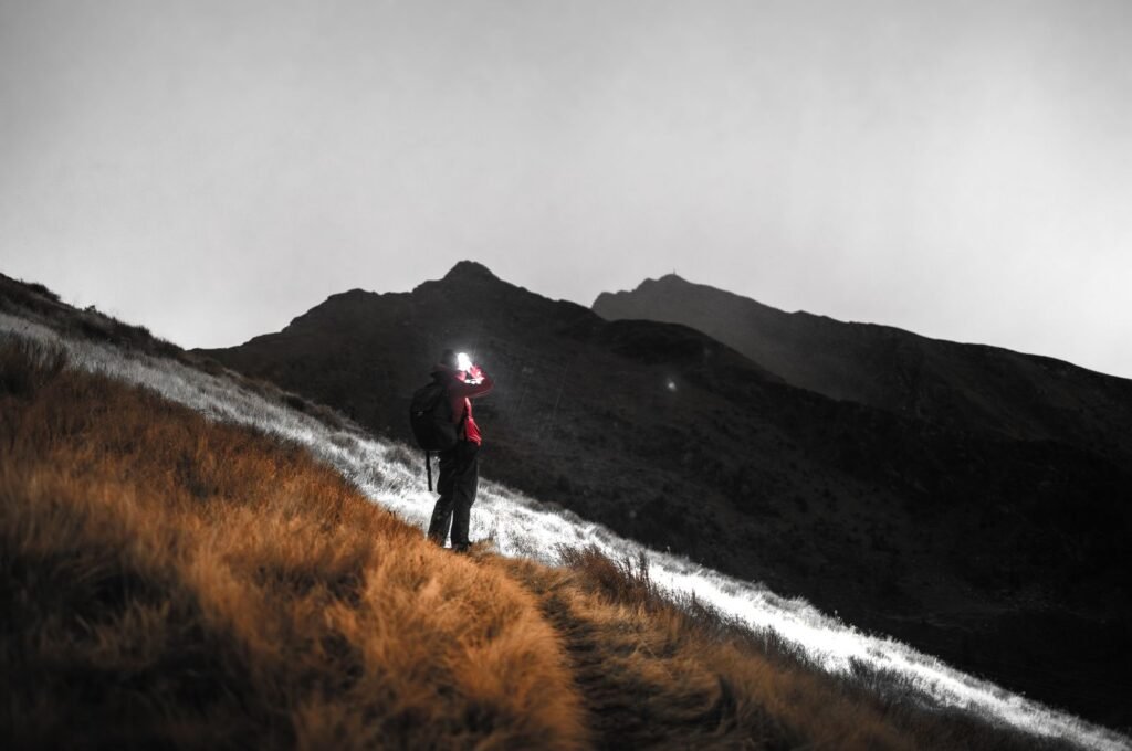 Traileur éclairé par sa lampe frontale sur un sentier de montagne la nuit