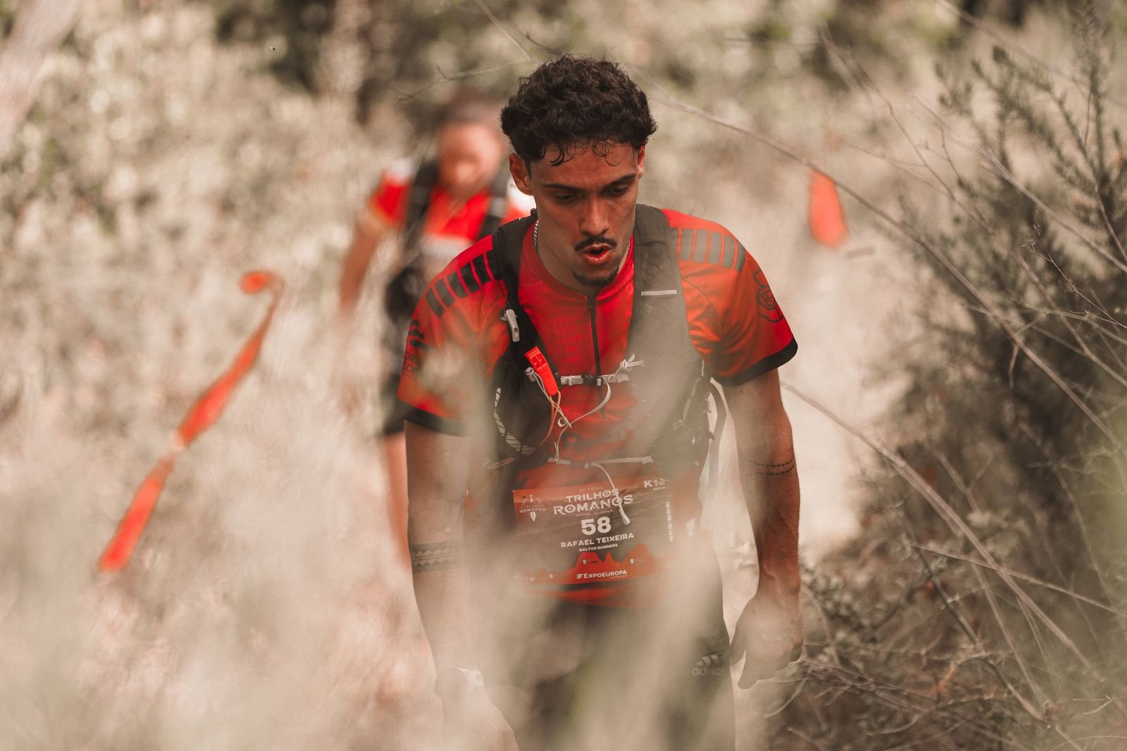 Coureur de trail progressant dans une montée sur un sentier étroit et caillouteux