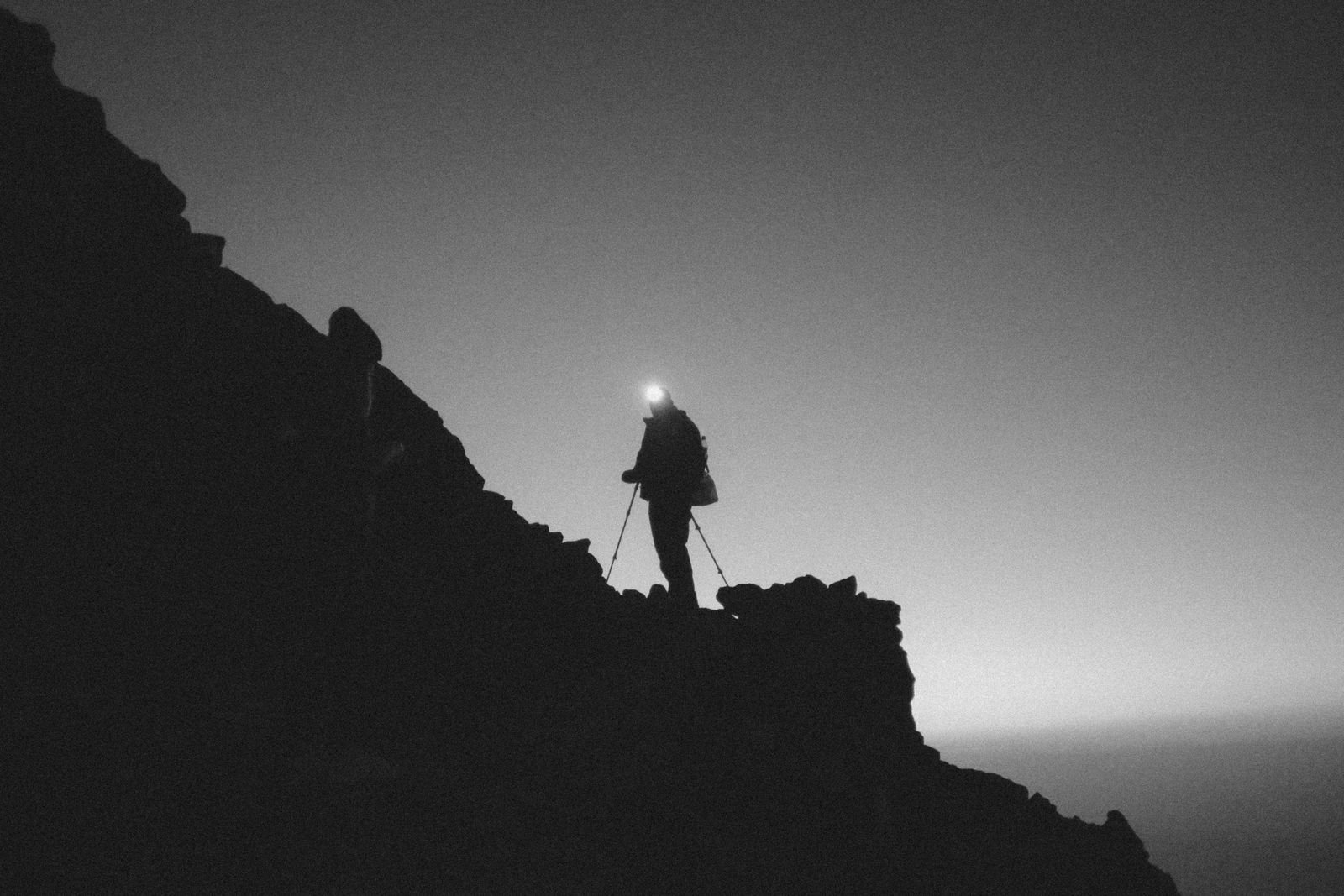 Coureur en silhouette sur une crête rocheuse de nuit, faisceau de frontale vers le sentier
